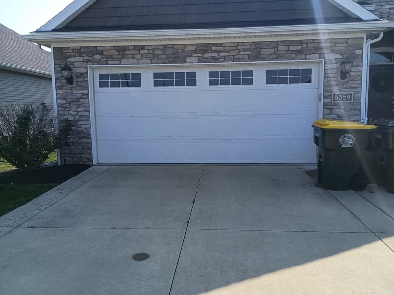 White carriage-style double garage door with windows on a stone-front home