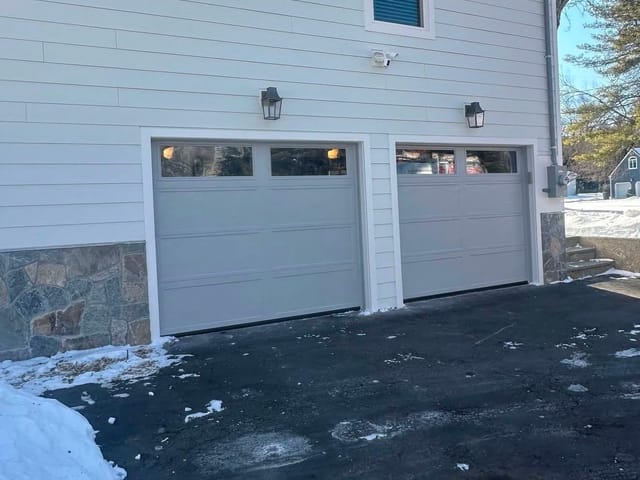 Two matching light-gray carriage-style garage doors with windows on a home with a stone base