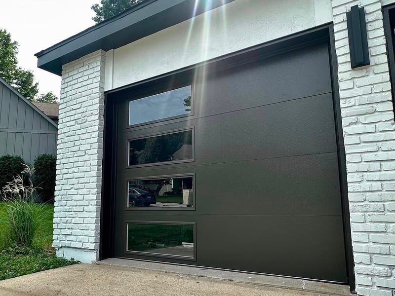 A new black modern flush-panel garage door with a vertical column of windows, set between white painted brick pillars