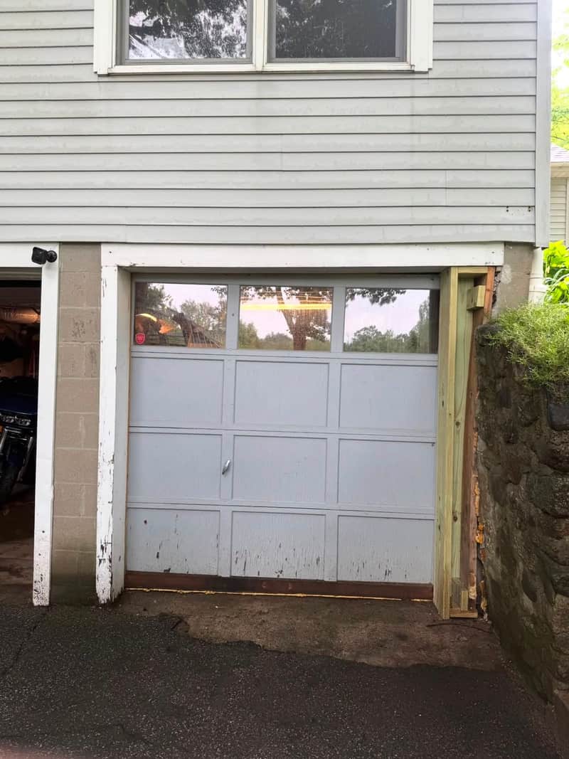 Worn light-blue raised-panel single garage door with peeling paint, before replacement